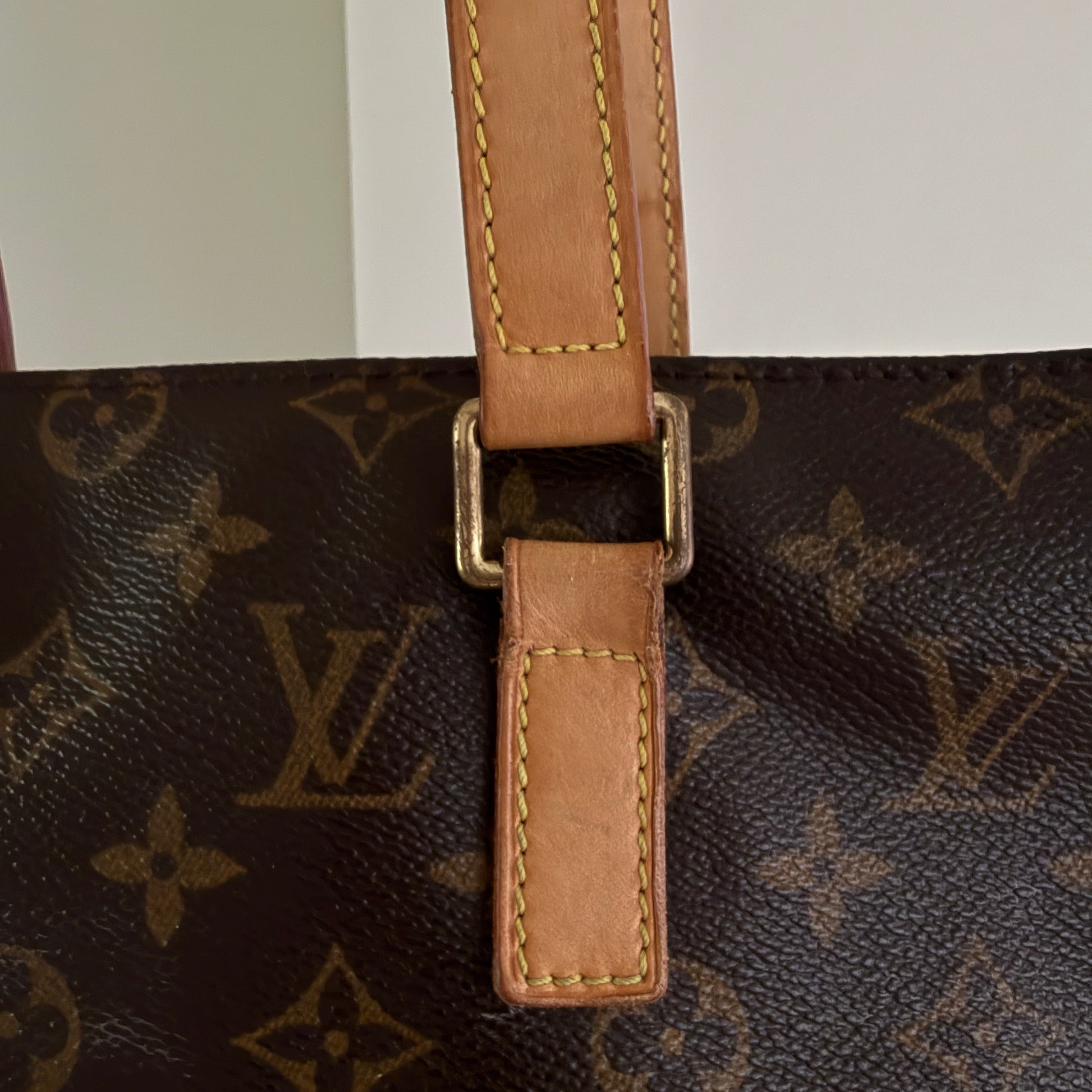 Close-up of a brown leather strap with gold buckle on a Louis Vuitton monogram bag.