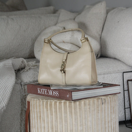 Beige handbag on a book with 'Kate Moss' branding on a textured ottoman in a living room setting.